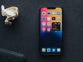 iPhone mit aktivem Bildschirm vor schwarzem Hintergrund und neben zerknülltem Papier.
