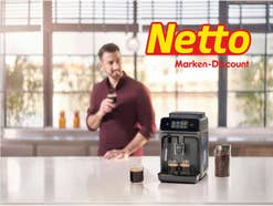 Ein Mann steht mit einem Kaffee in der Küche. Davor ist ein Philips Kaffeevollautomat und ein netto Logo zu sehen.