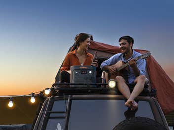 Jackery Explorer 2000 v2 auf einem Autodach, während jemand Gitarre spielt und eine weitere Person zuhört.