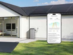 Ein Solarspeicher steht an einer Hauswand und eine App zeigt die Stromerzeugung.