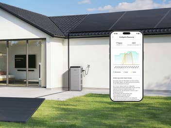 Ein Solarspeicher steht an einer Hauswand und eine App zeigt die Stromerzeugung.