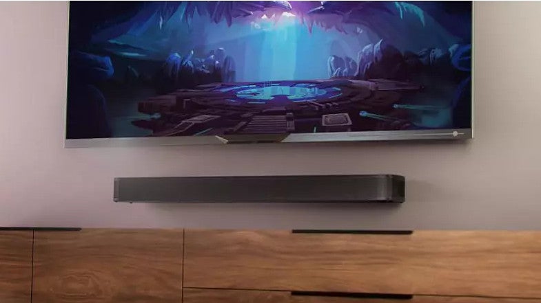 Die Soundbar JBL Bar 5.0 Multibeam auf einem Schränkchen unter einem Fernsehgerät.