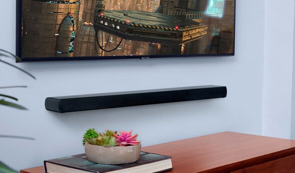 JBL Soundbar Cinema SB120 hängt in einem Wohnzimmer an einer Wand unter einem Fernseher.