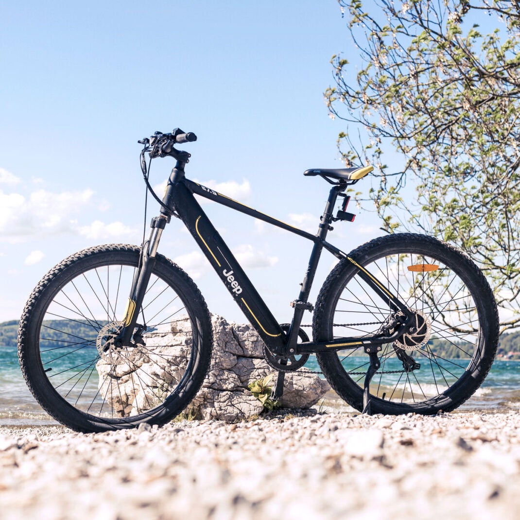 Das Jeep Mountain E-Bike MHR 7000 steht vor einem Felsbrocken an einem See.