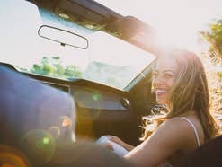 Frau sitzt auf dem Beifahrersitz eines Cabriolets und lacht im Sonnenlicht.