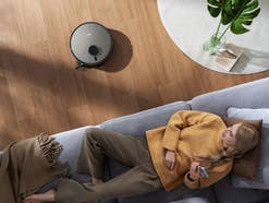 Frau liegt auf dem Sofa Jonr Saugroboter fährt