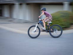 Ein Junge mit Helm saust auf einem Mountainbike um eine Ecke.