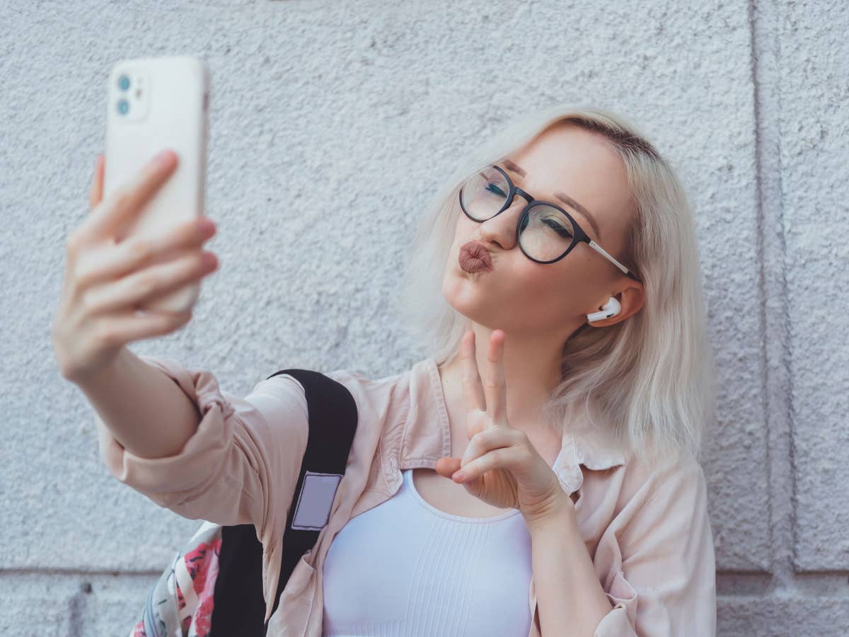 Junge blonde Frau mit iPhone und AirPods macht ein Selfie