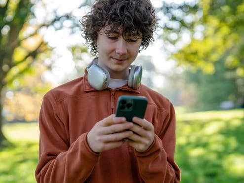 Junge Person steht in einem Park und schaut auf sein Smartphone
