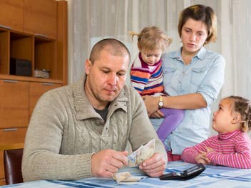 Betrübe Familie, Vater, Mutter und zwei Kinder mit Geldscheinen in den Händen des Vaters