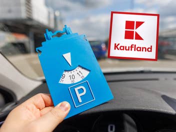 Ein Autofahrer hält eine Parkscheibe in der Hand, im Hintergrund ist ein Parkplatz und das Kaufland-Logo zu sehen