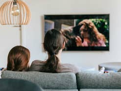 Ein Erwachsener und ein Kind sitzen auf dem Sofa und gucken TV.