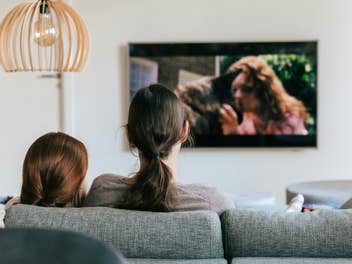 Ein Erwachsener und ein Kind sitzen auf dem Sofa und gucken TV.