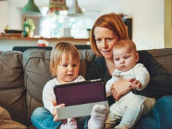 Mutter sitzt auf dem Sofa mit zwei Kindern und schaut auf ein Tablet