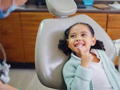 Kind beim Zahnarzt zeigt auf seine Zähne.