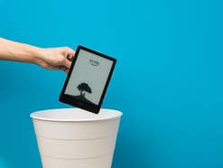 Eine Hand hält einen Kindle-Reader von Amazon über einem Mülleimer