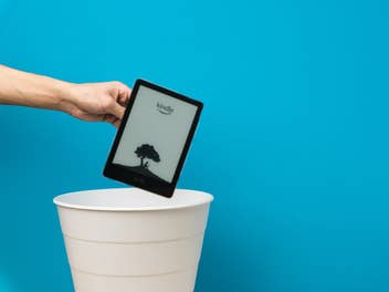 Eine Hand hält einen Kindle-Reader von Amazon über einem Mülleimer