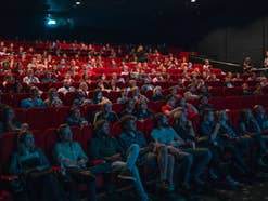 Viele Menschen in einem Kinosaal in roten Sesseln.