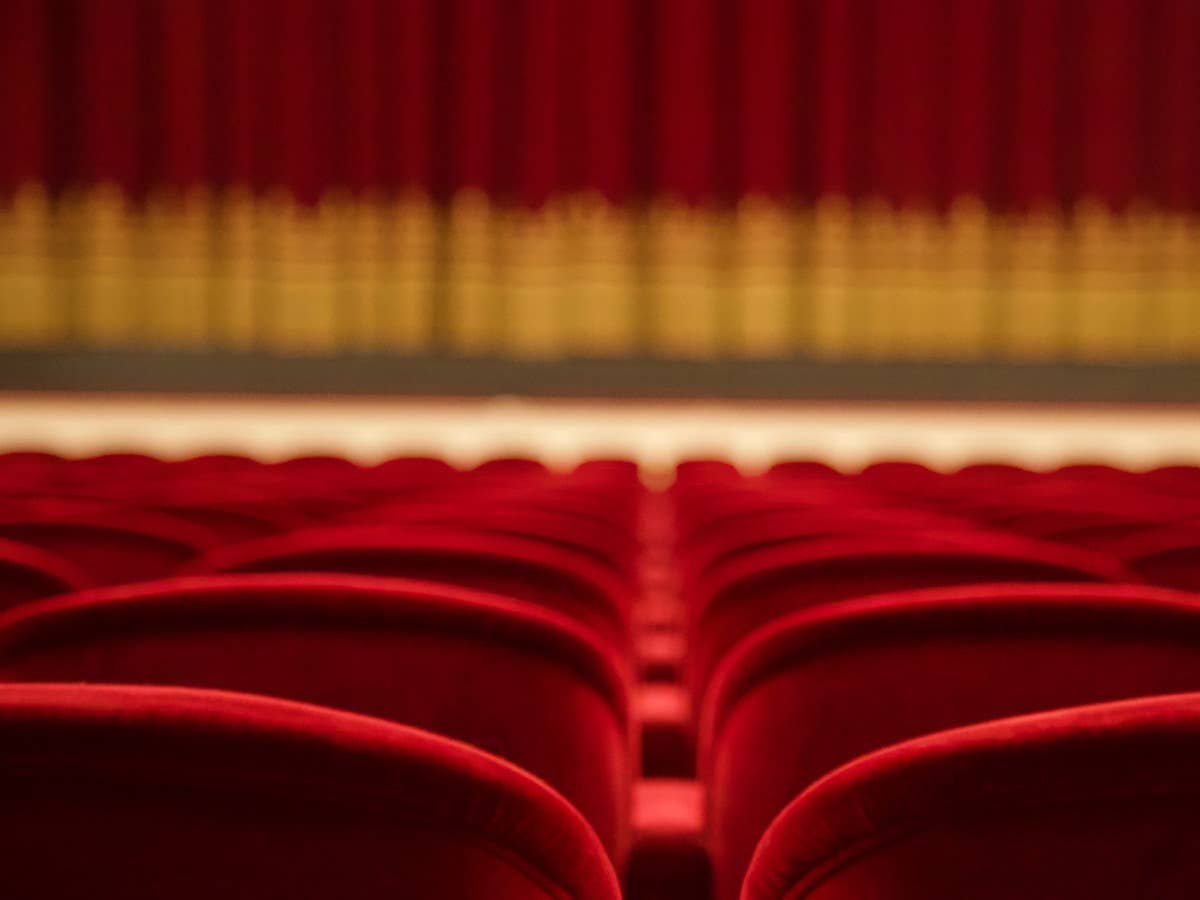 Rote Kinostühle in einem Kino, im Hintergrund verschwommen der Leinwandvorhang.