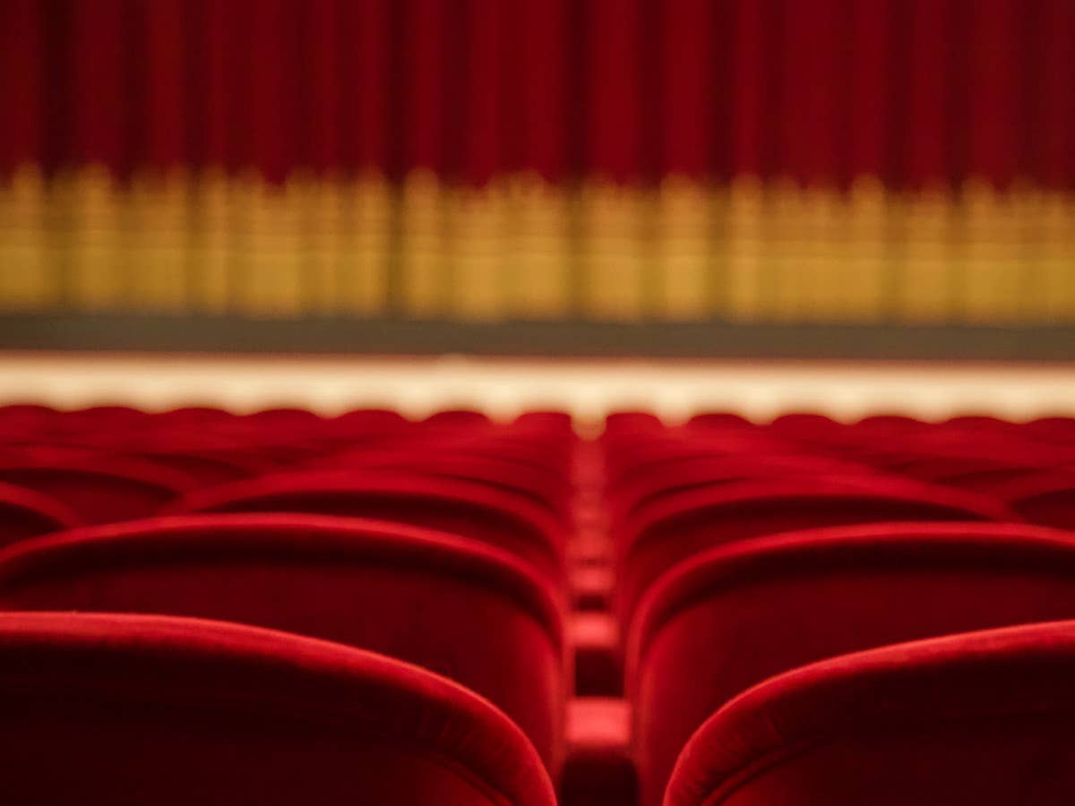 Rote Kinostühle in einem Kino, im Hintergrund verschwommen der Leinwandvorhang.