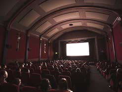 Menschen schauen einen Film aus den 1940er Jahren in einem alten Kinosaal.