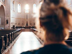 Frau steht in der Kirche und blickt in Richtung Altar.