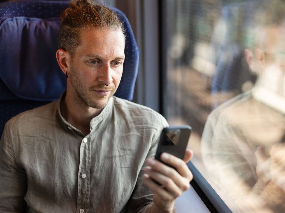 Ein Reisender nutzt ein Smartphone im ICE 3neo mit mobilfunkdurchlässiger Scheiben