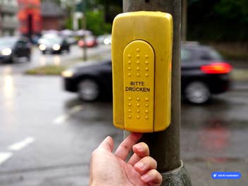 Hand drückt auf einen Knopf unter einem Ampelkasten