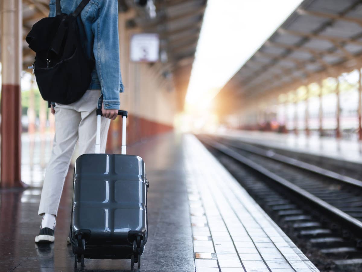 Ein junger Mann mit einem Koffer wartet am Bahnhof auf einen Zug, um zu reisen.