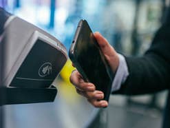 Eine Person hält ein Handy an eine Kasse, um per NFC zu zahlen.