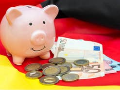 Sparschwein vor dem Hintergrund einer Deutschland-Flagge neben Euromünzen und Geldnoten.