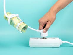 Stromkabel, das um Euroschein liegt und in Steckdose gesteckt wird