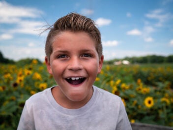 Ein lachener, frech dreinschauender Junge vor einem Sonnenblumenfeld
