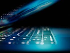 Halb zugeklappter Laptop Ein halb zugeklappter Laptop mit aktivem Bildschirm, der die Tastatur anleuchtet.