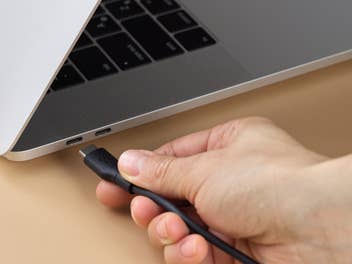 Eine Hand hält ein USB-C-Kabel an einen Laptop.