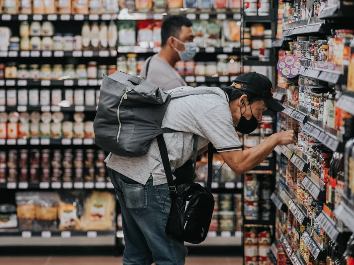 Ein Mann beugt sich zu einem Produkt, das sich im Supermarktregal befindet.