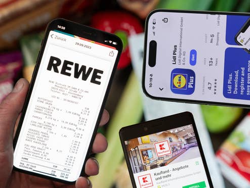 Was können die Apps von Lidl, Rewe, Kaufland & Co.? Lebensmittel, Kassenbon und eine Hand die eins von insgesamt drei Smartphones hält, auf denen die Apps von Rewe, Lidl und Kaufland geöffnet sind