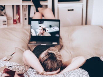 Eine junge Frau liegt auf dem Bett, hat einen Laptop auf den Beinen und streamt Filme.