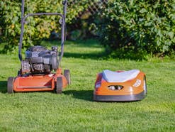Ein Rasenmäher und ein Mähroboter nebeneinander auf dem Rasen