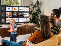 Eine Familie sitzt vor einem Fernseher auf dem das Menü von Magenta TV zu sehen ist