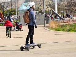 Ein Mann mit Helm fährt mit einem E-Skateboard über einen Platz.