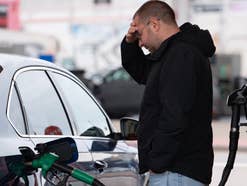 Ein Mann steht vor seinem Auto und hält sich den Kopf, während die Zapfsäule das Gefährt betankt.
