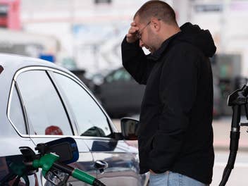 Ein Mann steht vor seinem Auto und hält sich den Kopf, während die Zapfsäule das Gefährt betankt.