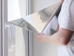Mann bringt UV-Sonnenschutzfolie am Fenster an