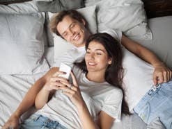 Mann und Frau liegen im Bett und schauen auf ein Smartphone
