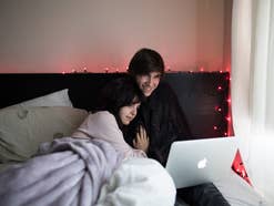Eine junge frau und ein junger Mann kuscheln in einem Bett und schauen einen Film auf einem Laptop.