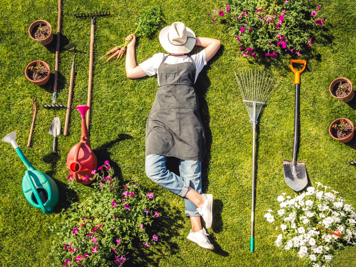 Ein Mann liegt im Garten zwischen Pflanzen und Geräten