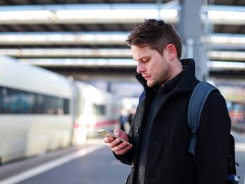 Mann mit einem Smartphone am Bahnhof