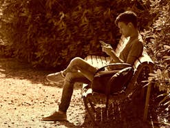 Handynutzung im Park Ein Mann sitzt auf einer Parkbank und nutzt sein Handy