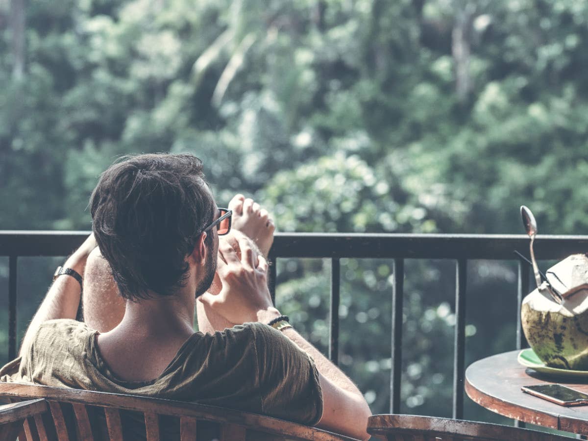 Ein Mann sitzt auf einem Balkon ohne Handy, neben sich eine offene Kokosnuss.